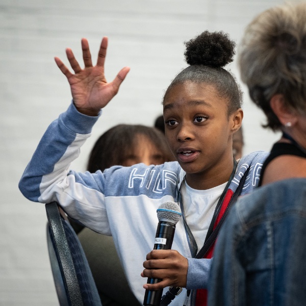 A student waves her hand as she speaks into a microphone