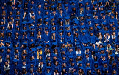 A view from above of graduates in blue gowns sitting.