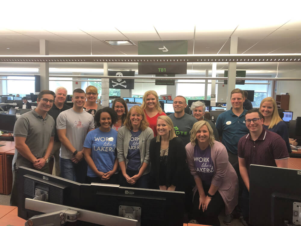 Two rows of people standing in an open room with computer monitors