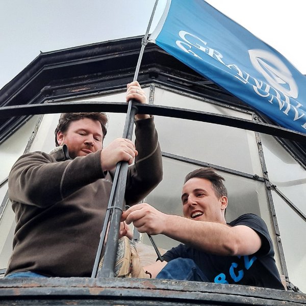 two people attaching a Grand Valley State University flag near the top of a lighthouse