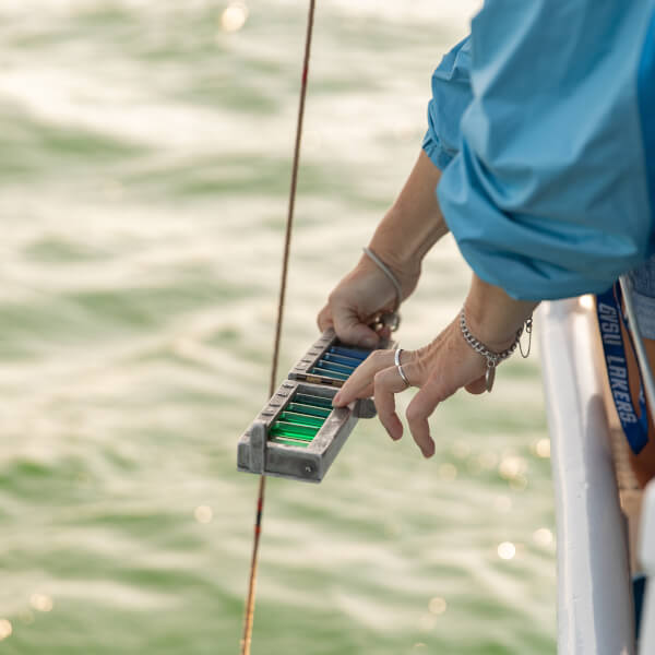 A passenger on a GVSU research vessel holds up water samples to analyze the color of Lake Michigan, in the background.