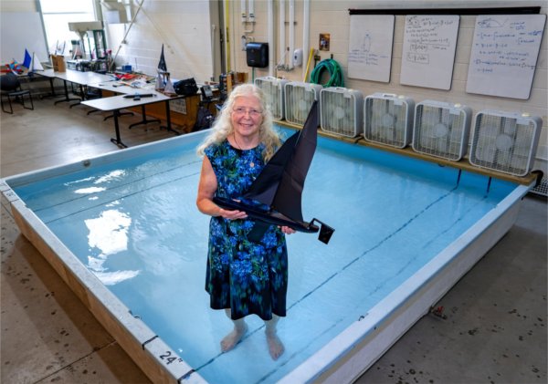 Shirley Fleischmann, professor of engineering, stands in a shallow pool holding a model sailboat