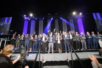 large group of people on stage holding awards, blue spotlights in back