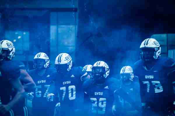 Lakers football team runs on to the field through a cloud of blue smoke