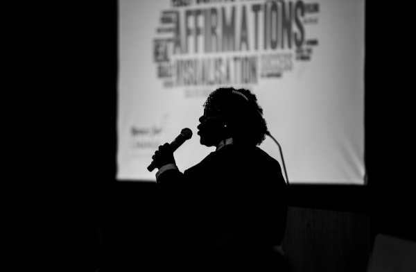 A speaker is silhouetted with a microphone against a screen during a summit.