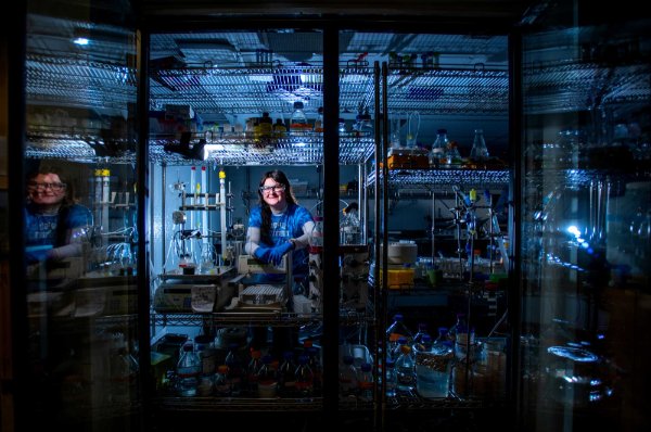 A college student wearing safety glasses poses for a portrait in a cold room of a biochemistry lab. 