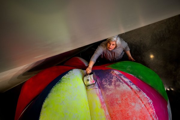 A person looks up toward the camera while positioning a giant piece of art made out of an inflated ball of brightly colored fabric. 