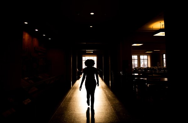 A silhouetted person walks into a beam of warm light coming through a doorway. 