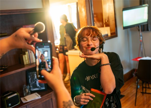  A college student poses with their hand under their chin for a cellphone photo while on a movie set. 