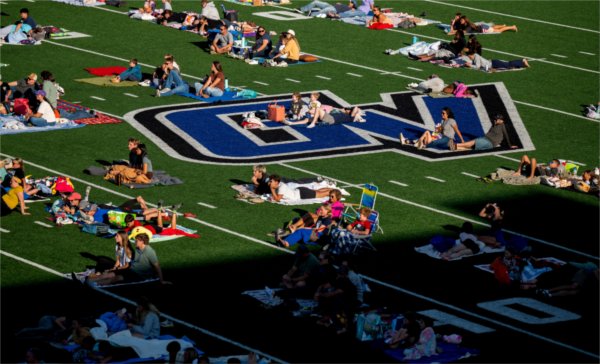 Families and friends lay on a football field with a GV logo in the center in preparation for a movie. 
