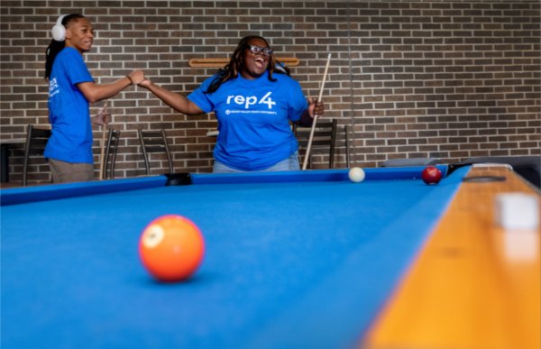 Two high-school students high five and laugh together as they play a game of pool. 