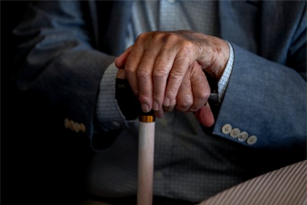  Hands from a person wearing a suit rests on a cane. 