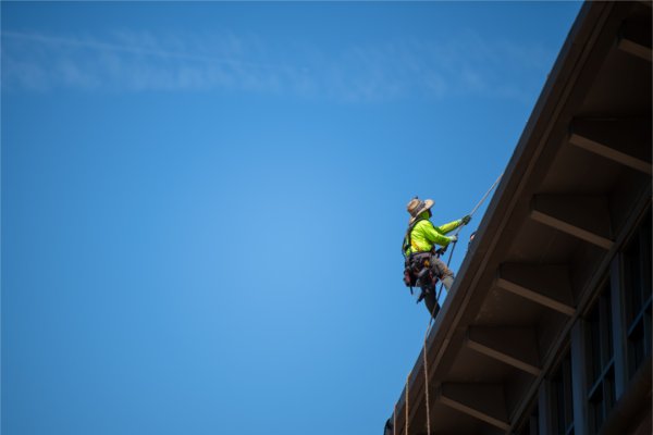  A worker wearing safety gear works on the roof of a building with a blue sky in the background. 