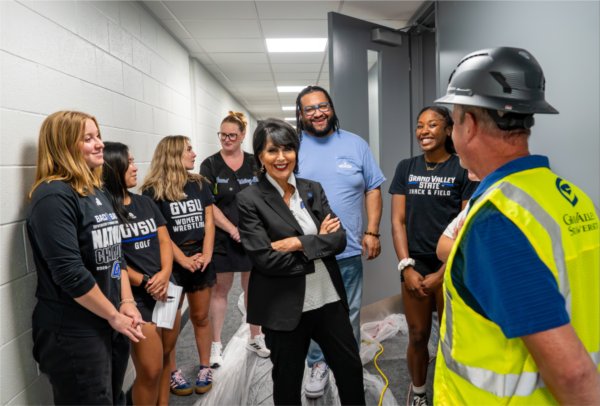  A university president stands among a group of student athletes, a construction worker and a senior leadership member. 