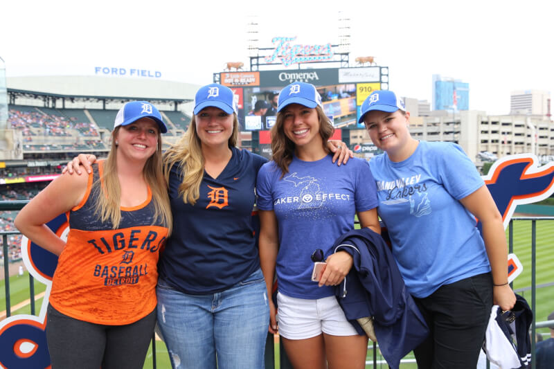 Three GVSU alumni standing and smiling with the baseball field behind them