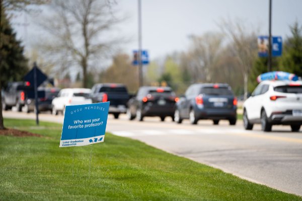 Cars pass by a sign that says: "GVSU Memories. Who was your favorite professor? Laker Graduation Celebration