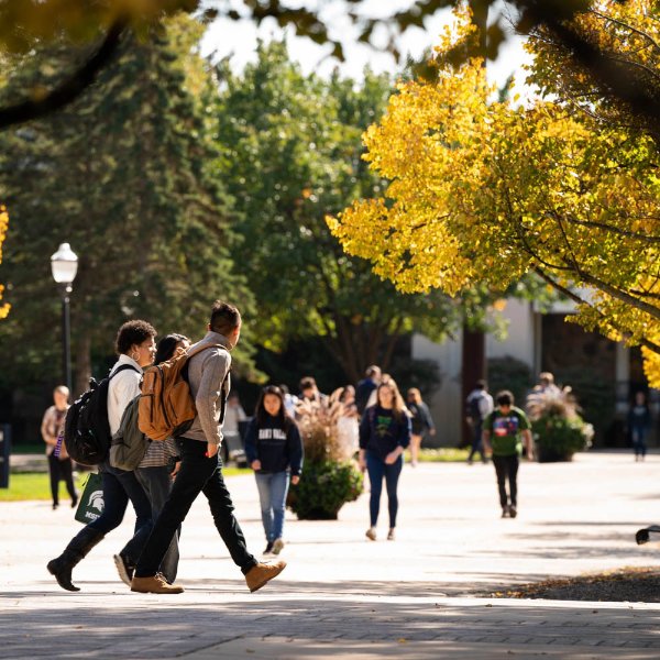 Students walking on the sidewalk on the Allendale campus, trees in fall colors, some still green