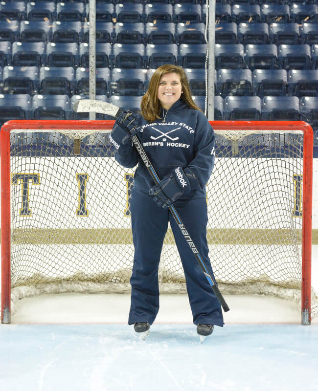 woman in goalie equipment, ice skates in front of net