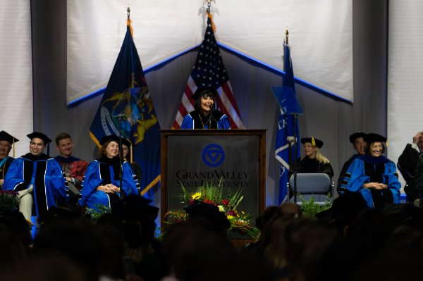 President Mantella offers remarks from a podium on stage, all platform party wearing academic regalia