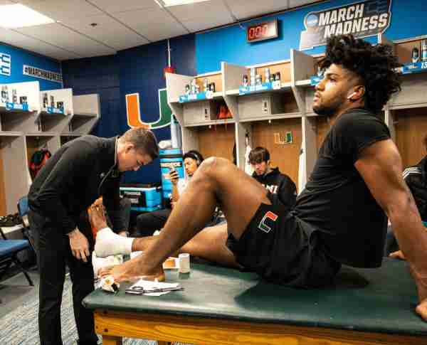 Sam Johnson tapes the ankle of Miami basketball player Norchad Omier prior to a NCAA Tournament game.