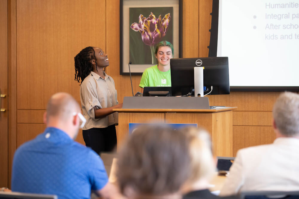 two women standing in front of room giving presentation