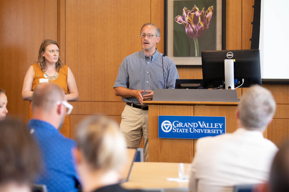 woman and man at front of room, giving presentation