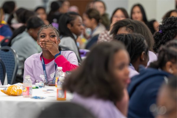 people at tables, girl in center with mouth over hand reacting