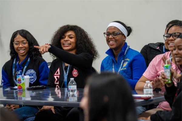 four people seated at table, woman second from left pointing