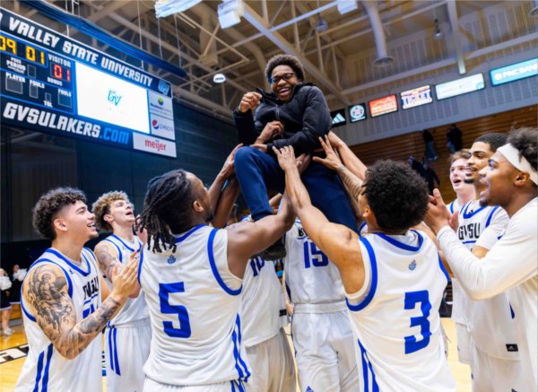 A men's college basketball team in white and blue jerseys hoist a young smiling child over their head.