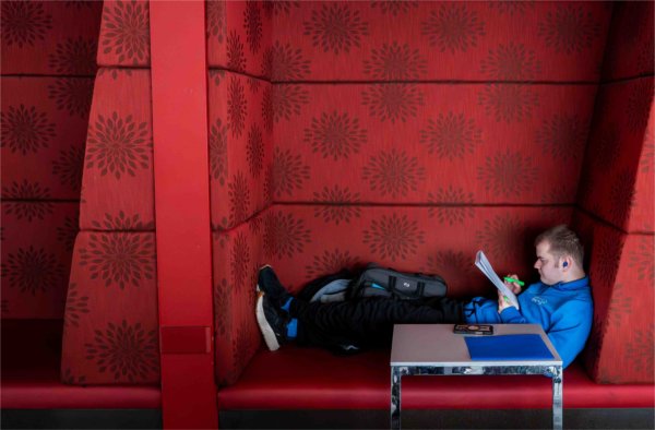A college student in blue works on homework inside a red alcove of a study room. 