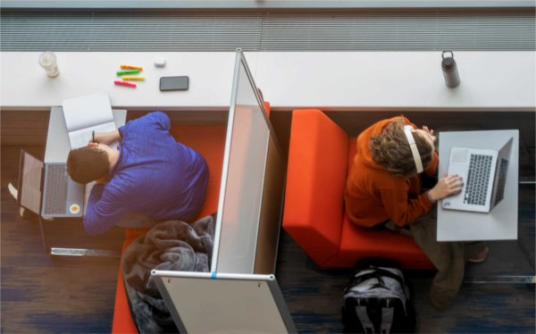 Two college students are seen from above working on their laptop computers. 