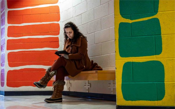 A person sits on a bench among colorful artwork murals on the walls nearby. 