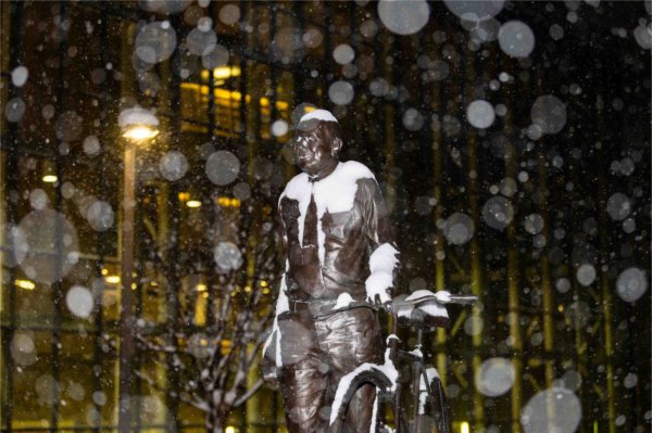 Snowfall surrounds a bronze sculpture outside on a college campus.  