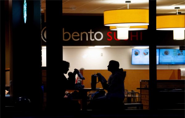 Silhouettes of college students enjoying breakfast together near a window.  