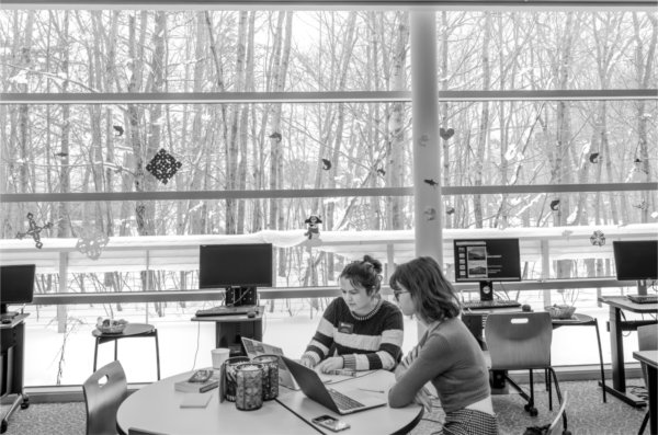  With a window that showcases a wooded area, people work in a writing center on a college campus. 