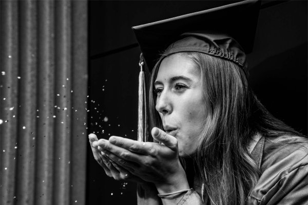 A student wearing a cap and gown blows glitter from her hands. 