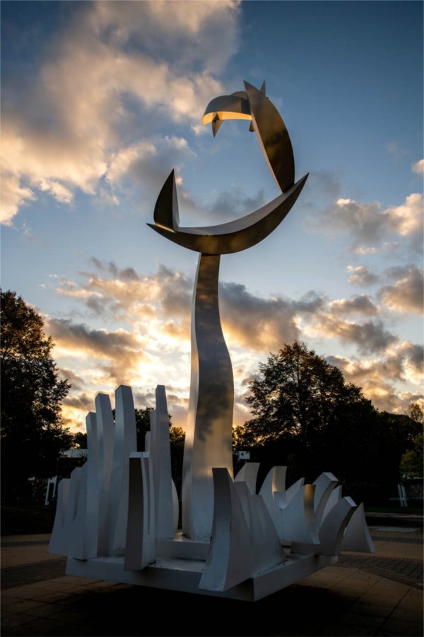 An art sculpture is seen against a blue and cloudy morning sky. 