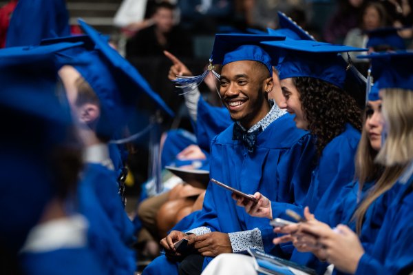 A group of college students laugh as they wear their cap and gowns. 