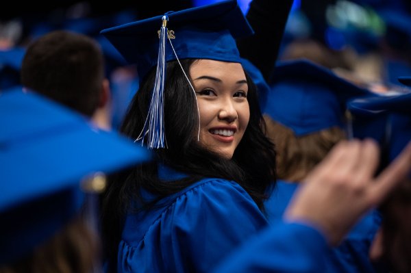  A college student looks over a shoulder wearing a blue cap and gown during commencement.