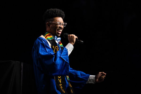 A college student sings the national anthem wearing Commencement attire.   