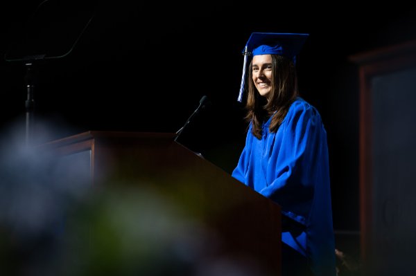  A college student speaks at the lectern in her blue cap and gown.