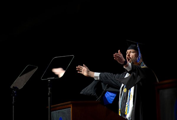  A person wearing a cap and gown speaks at a podium.