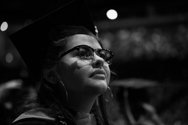  A college student wearing glasses and cap and gown listens during Commencement speeches. 