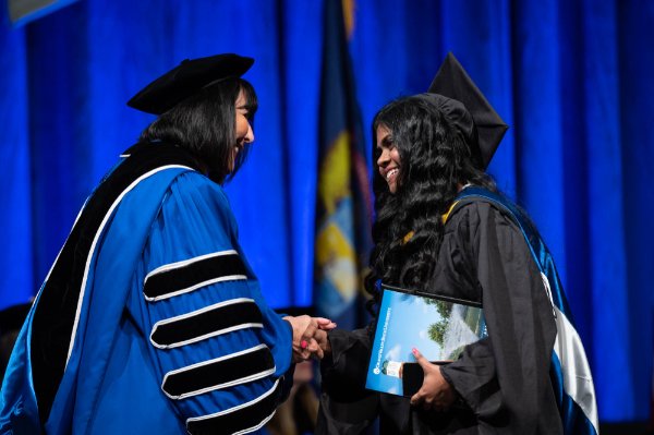  A university president shakes the hand of a college graduate after they received their diploma.