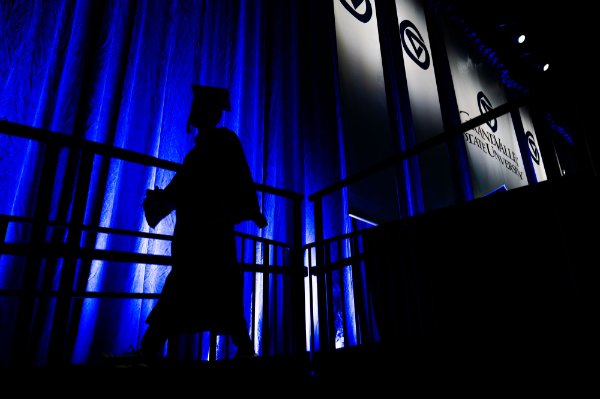  A college student is silhouetted against a blue curtain as they exit the stage during Commencement. 