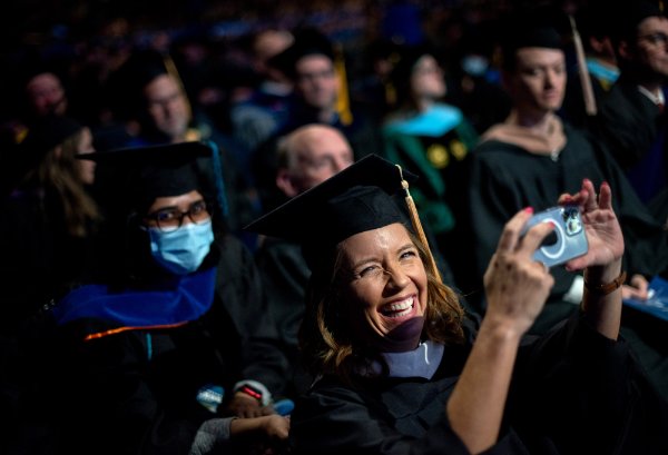 A university faculty member laughs as she takes a photo as a student walks across the stage during Commencement.  