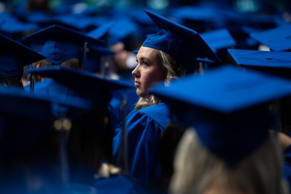  A college student wearing a blue cap and gown is framed by other graduates during commencement ceremonies. 