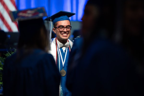  A college student wearing graduation attire poses for a photo. 
