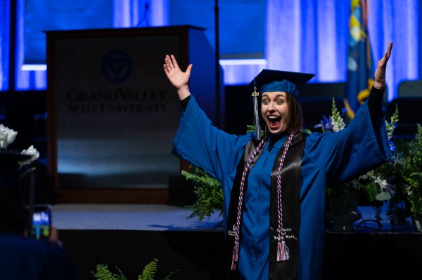  A college student poses with arms raised for a photo during commencement.