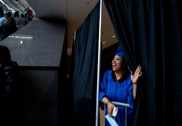  A college student peeks from behind a curtain to look for family during Commencement. 